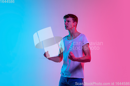 Image of Young caucasian man\'s portrait on gradient blue-pink studio background in neon light