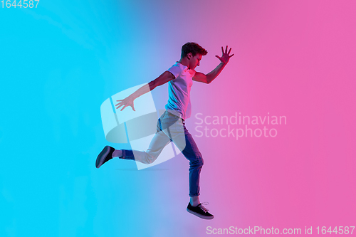 Image of Young caucasian man\'s jumping high on gradient blue-pink studio background in neon light