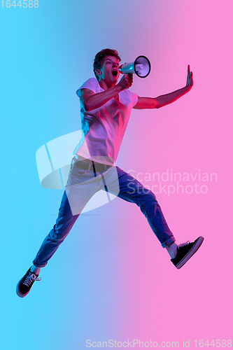 Image of Young caucasian man\'s jumping high on gradient blue-pink studio background in neon light