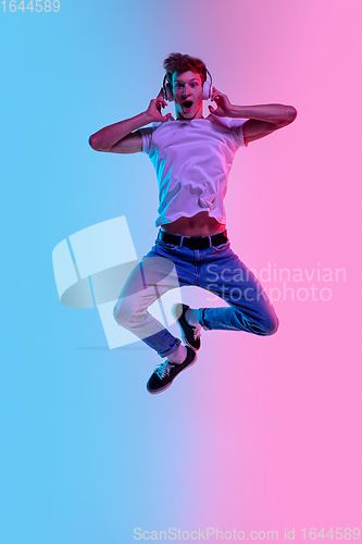 Image of Young caucasian man\'s jumping high on gradient blue-pink studio background in neon light