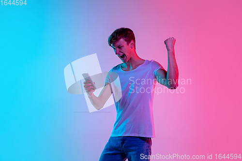 Image of Young caucasian man\'s portrait on gradient blue-pink studio background in neon light