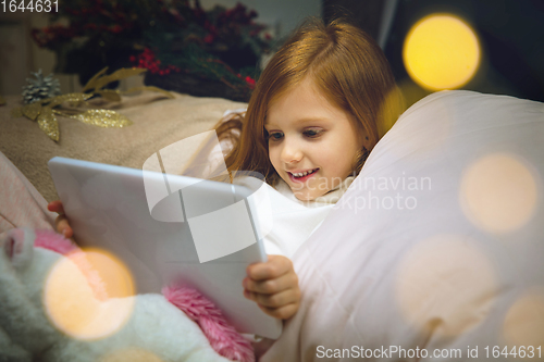 Image of Happy caucasian little girl during video call or messaging with Santa using laptop and home devices, looks delighted and happy