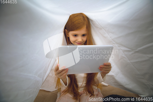 Image of Happy caucasian little girl during video call or messaging with Santa using laptop and home devices, looks delighted and happy