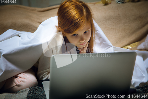 Image of Happy caucasian little girl during video call or messaging with Santa using laptop and home devices, looks delighted and happy