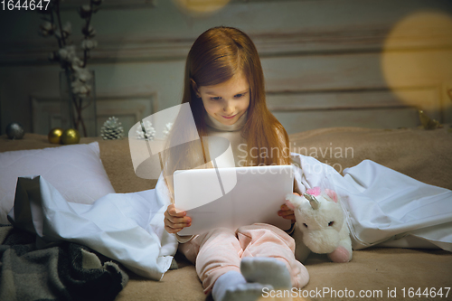 Image of Happy caucasian little girl during video call or messaging with Santa using laptop and home devices, looks delighted and happy