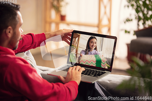 Image of Celebration and holidays during quarantine concept. Friends or family unpacking gifts while talking using video call