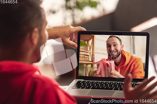 Image of Celebration and holidays during quarantine concept. Friends or family unpacking gifts while talking using video call