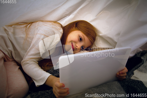 Image of Happy caucasian little girl during video call or messaging with Santa using laptop and home devices, looks delighted and happy