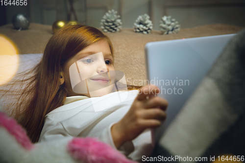 Image of Happy caucasian little girl during video call or messaging with Santa using laptop and home devices, looks delighted and happy