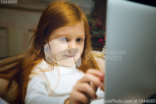 Image of Happy caucasian little girl during video call or messaging with Santa using laptop and home devices, looks delighted and happy