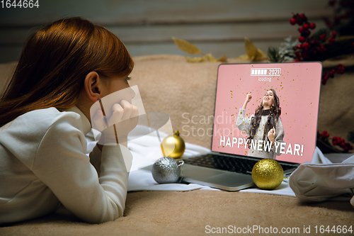 Image of Happy caucasian little girl during video call or messaging with Santa using laptop and home devices, looks delighted and happy