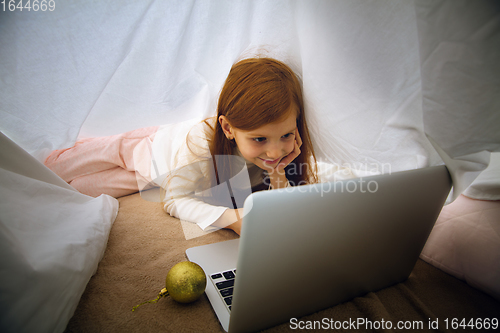 Image of Happy caucasian little girl during video call or messaging with Santa using laptop and home devices, looks delighted and happy