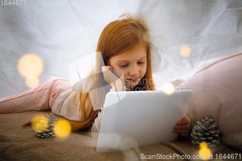 Image of Happy caucasian little girl during video call or messaging with Santa using laptop and home devices, looks delighted and happy