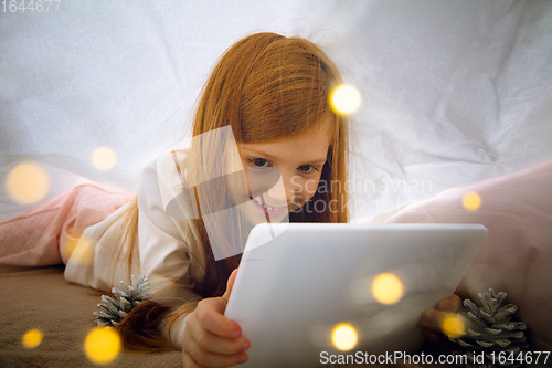 Image of Happy caucasian little girl during video call or messaging with Santa using laptop and home devices, looks delighted and happy