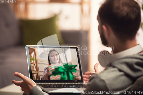 Image of Celebration and holidays during quarantine concept. Friends or family unpacking gifts while talking using video call