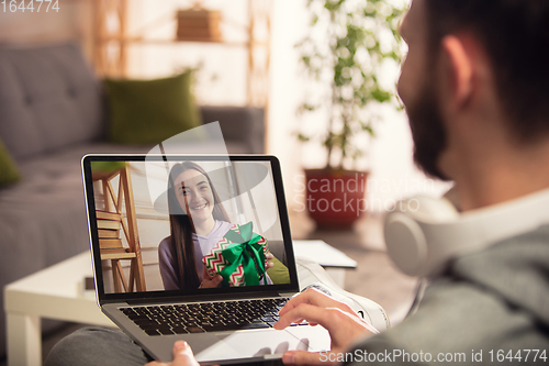 Image of Celebration and holidays during quarantine concept. Friends or family unpacking gifts while talking using video call