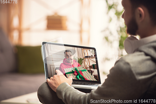 Image of Celebration and holidays during quarantine concept. Friends or family unpacking gifts while talking using video call