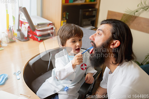 Image of Little boy playing pretends like doctor examining a man in comfortabe medical office