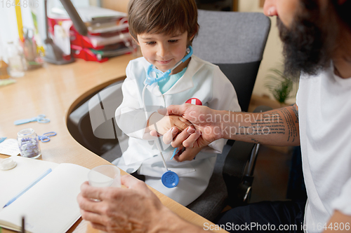 Image of Little boy playing pretends like doctor examining a man in comfortabe medical office