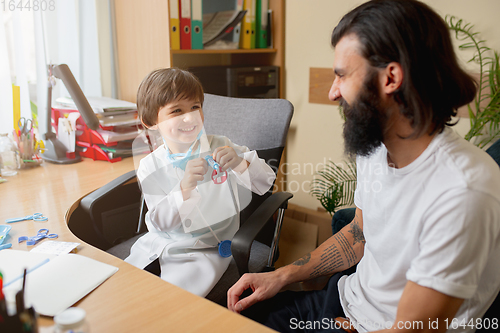 Image of Little boy playing pretends like doctor examining a man in comfortabe medical office