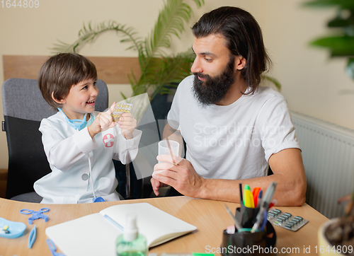 Image of Little boy playing pretends like doctor examining a man in comfortabe medical office