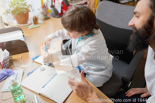 Image of Little boy playing pretends like doctor examining a man in comfortabe medical office