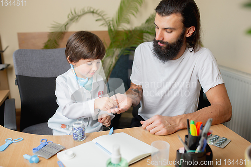 Image of Little boy playing pretends like doctor examining a man in comfortabe medical office