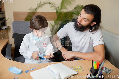 Image of Little boy playing pretends like doctor examining a man in comfortabe medical office