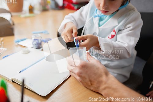 Image of Little boy playing pretends like doctor examining a man in comfortabe medical office