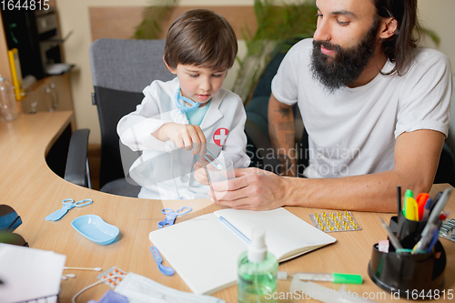 Image of Little boy playing pretends like doctor examining a man in comfortabe medical office