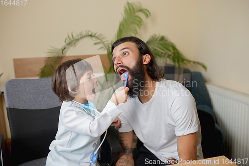 Image of Little boy playing pretends like doctor examining a man in comfortabe medical office