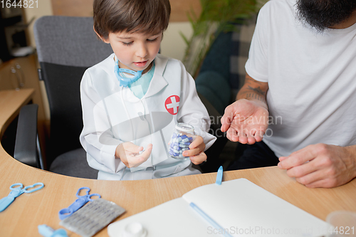 Image of Little boy playing pretends like doctor examining a man in comfortabe medical office