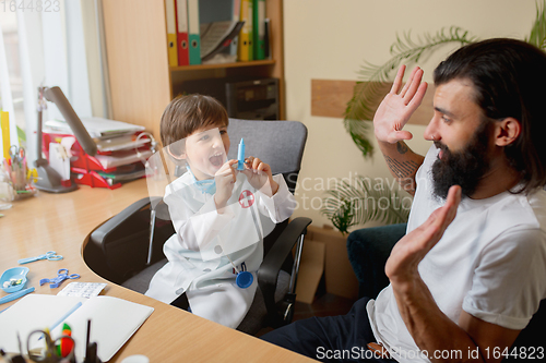 Image of Little boy playing pretends like doctor examining a man in comfortabe medical office