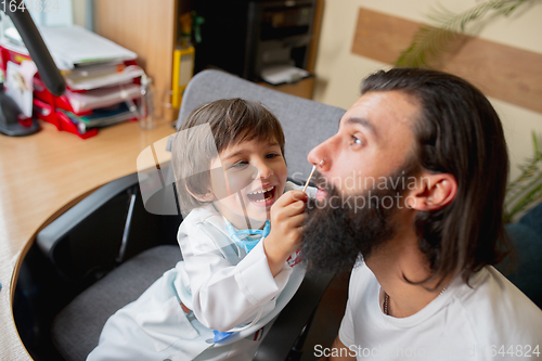 Image of Little boy playing pretends like doctor examining a man in comfortabe medical office