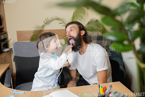 Image of Little boy playing pretends like doctor examining a man in comfortabe medical office