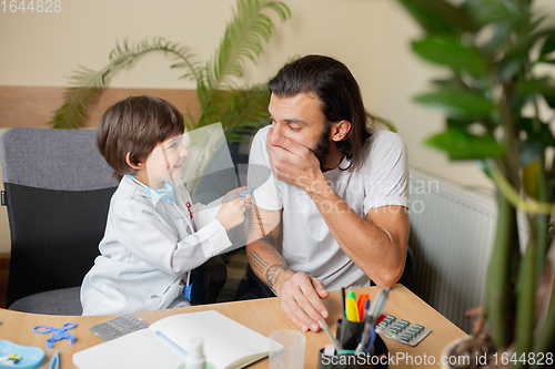 Image of Little boy playing pretends like doctor examining a man in comfortabe medical office