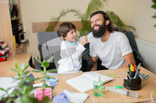 Image of Little boy playing pretends like doctor examining a man in comfortabe medical office