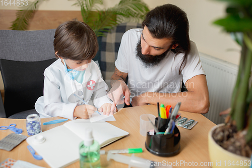 Image of Little boy playing pretends like doctor examining a man in comfortabe medical office