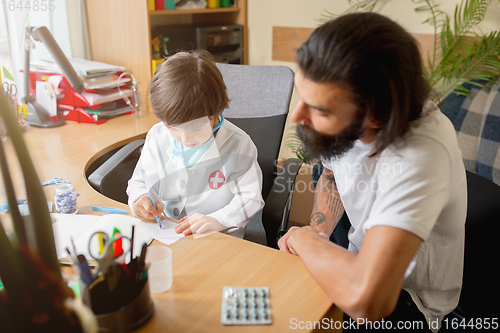 Image of Little boy playing pretends like doctor examining a man in comfortabe medical office