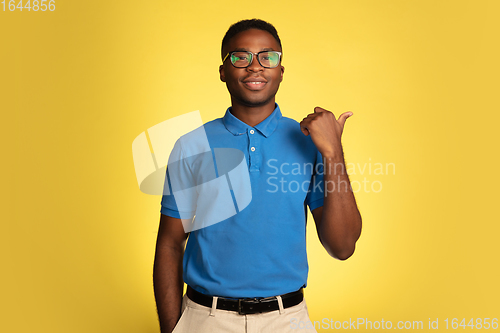 Image of Young african-american man\'s portrait isolated on yellow studio background, facial expression. Beautiful male half-lenght portrait with copyspace.