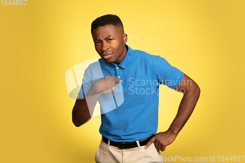 Image of Young african-american man\'s portrait isolated on yellow studio background, facial expression. Beautiful male half-lenght portrait with copyspace.