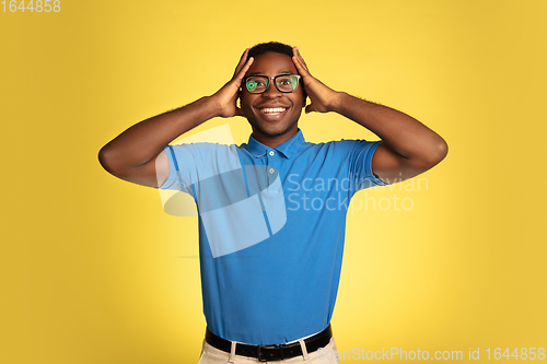 Image of Young african-american man\'s portrait isolated on yellow studio background, facial expression. Beautiful male half-lenght portrait with copyspace.