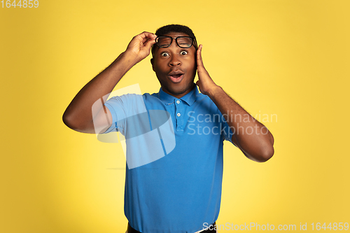 Image of Young african-american man\'s portrait isolated on yellow studio background, facial expression. Beautiful male half-lenght portrait with copyspace.