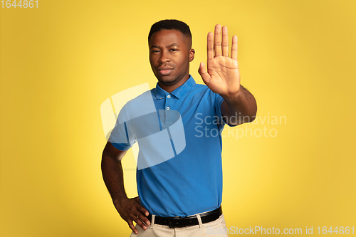 Image of Young african-american man\'s portrait isolated on yellow studio background, facial expression. Beautiful male half-lenght portrait with copyspace.