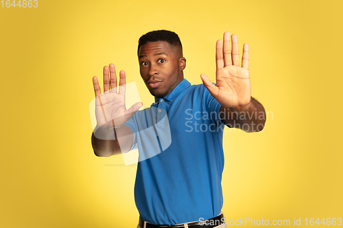 Image of Young african-american man\'s portrait isolated on yellow studio background, facial expression. Beautiful male half-lenght portrait with copyspace.