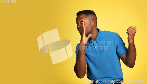 Image of Young african-american man\'s portrait isolated on yellow studio background, facial expression. Beautiful male half-lenght portrait with copyspace.