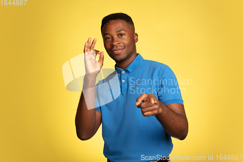 Image of Young african-american man\'s portrait isolated on yellow studio background, facial expression. Beautiful male half-lenght portrait with copyspace.