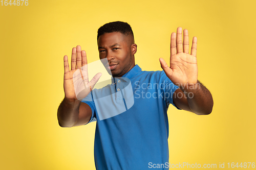 Image of Young african-american man\'s portrait isolated on yellow studio background, facial expression. Beautiful male half-lenght portrait with copyspace.