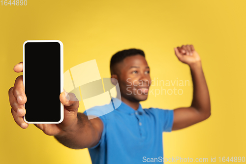 Image of Young african-american man\'s portrait isolated on yellow studio background, facial expression. Beautiful male half-lenght portrait with copyspace.