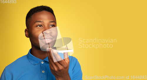 Image of Young african-american man\'s portrait isolated on yellow studio background, facial expression. Beautiful male half-lenght portrait with copyspace.